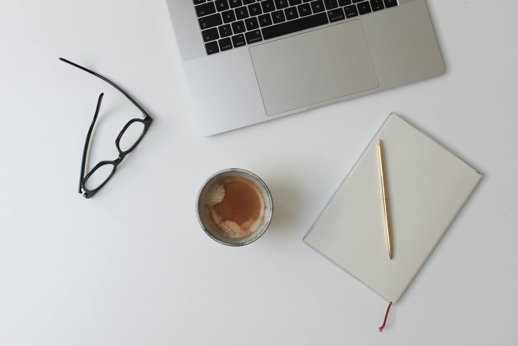Minimalist flat lay of a workspace with a laptop, coffee, glasses, and notepad.